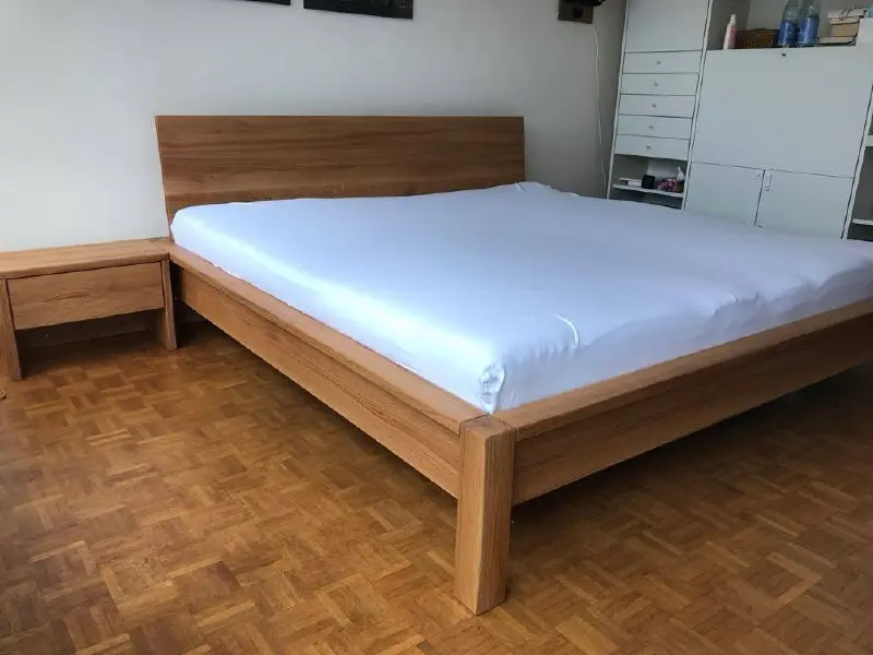 Fertiges Massivholzbett mit geradem Kopfteil, klarer Rahmenkonstruktion und passendem Nachttisch