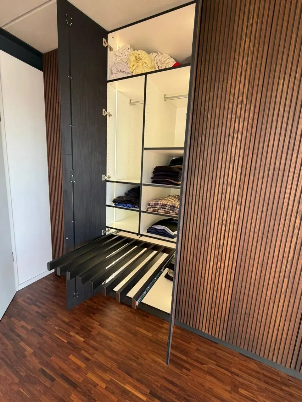 Geöffnete Schrankfächer mit gefalteter Kleidung und ausgezogenem Hosenhalter